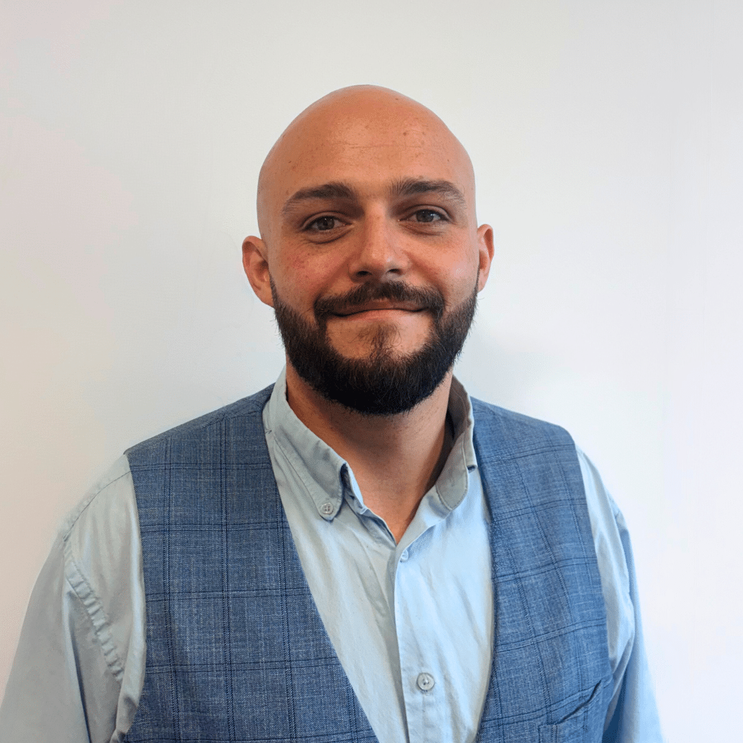 Portrait d’un homme souriant en gilet et chemise devant un fond clair