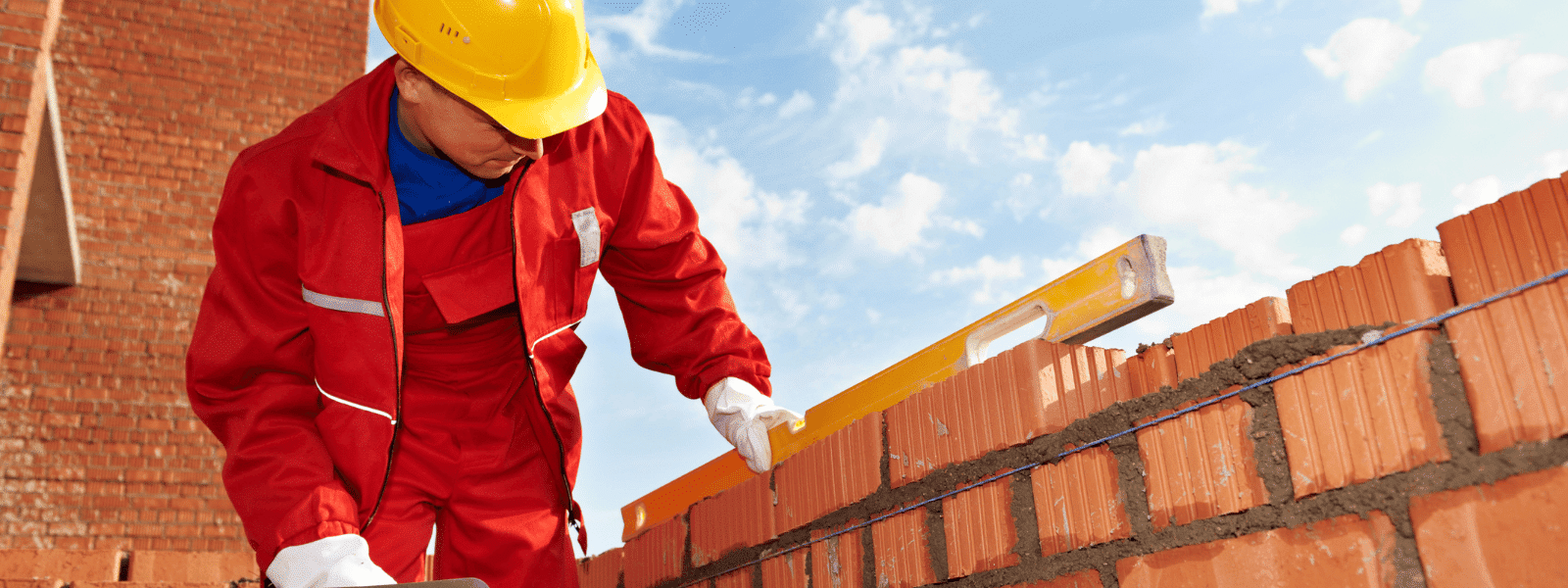 Ouvrier du bâtiment utilisant une règle sur un mur de briques rouges